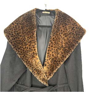 Peut inclure: Manteau noir avec un col à imprimé léopard. Le manteau a un large col avec un imprimé animalier marron et noir. Le manteau est suspendu à un cintre noir sur fond blanc. Le manteau a une ceinture.