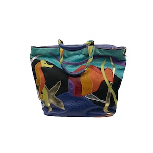 May include: A vibrant tote bag with a marine theme. The bag showcases a seahorse, starfish, and other sea-inspired designs in various colours, including blue, orange, and gold. The bag has braided handles and a textured surface.