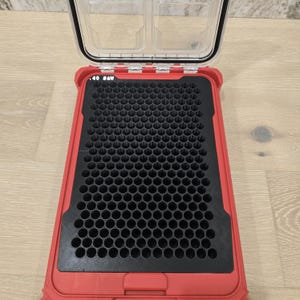 May include: A red rectangular storage case with an open clear lid, featuring a black interior insert with a dense grid of circular holes. The text 40 SAW is printed in white on the top left corner of the black insert within the red frame.