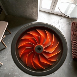 May include: A round, black and orange rug with a turbine design. The rug features a central hub with radiating orange blades, creating a dynamic, industrial aesthetic. The rug is set against a gray concrete floor.