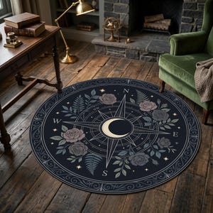 Puede incluir: Una alfombra circular con fondo azul marino que presenta un diseño de rosa de los vientos central, una luna creciente color crema e ilustraciones de rosas rosa pálido y hojas de helecho verdes, con pequeñas estrellas doradas y puntos cardinales.