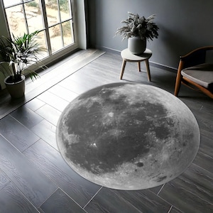 Pode incluir: Um tapete redondo cinza e branco com um design de lua. O tapete está em um piso de madeira escura.