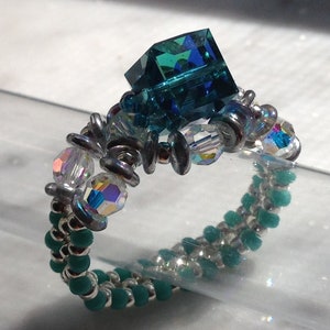May include: A teal blue crystal ring with silver beads and teal blue seed beads.
