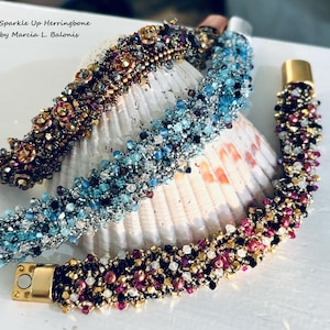 May include: Three beaded bracelets in shades of blue, gold, and burgundy. The bracelets are made with small beads and have gold-colored magnetic clasps. The bracelets are displayed on a seashell.