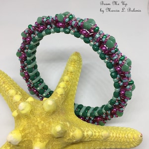 May include: A green, pink, and blue beaded bracelet with a spiral design. The bracelet is on a yellow starfish. The text "Beam Me Up by Marcia L. Balonis" is above the bracelet.