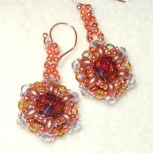 May include: A pair of dangle earrings with a copper and gold color scheme. The earrings feature a cluster of beads in a geometric pattern with a red crystal in the center.