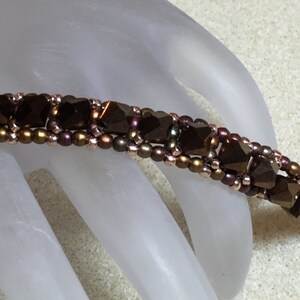 May include: A brown and gold beaded bracelet with a geometric pattern. The bracelet is made with small, faceted beads and is strung on a thin wire.