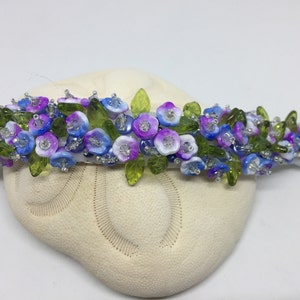 May include: A beaded bracelet with blue, purple, and white flowers and green leaves.
