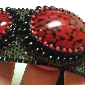 Op de afbeelding: Een zwarte en rode kralen armband met drie rode en zwarte gepatroneerde cabochons. De armband is gemaakt met een zwarte mesh basis en heeft een zwarte kralen rand.