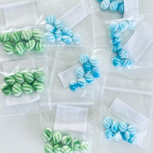 May include: Six clear plastic bags filled with small, swirl-patterned glass beads. The beads are in three colors: green, blue, and light blue.