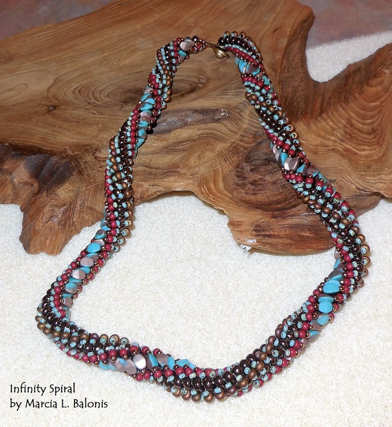 May include: A multi-colored beaded necklace with a spiral design. The necklace is made with brown, red, and turquoise beads. The necklace is called "Infinity Spiral" by Marcia L. Balonis.