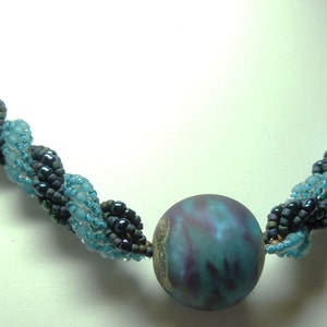 May include: A blue and black beaded necklace with a large, iridescent blue and purple bead in the center.