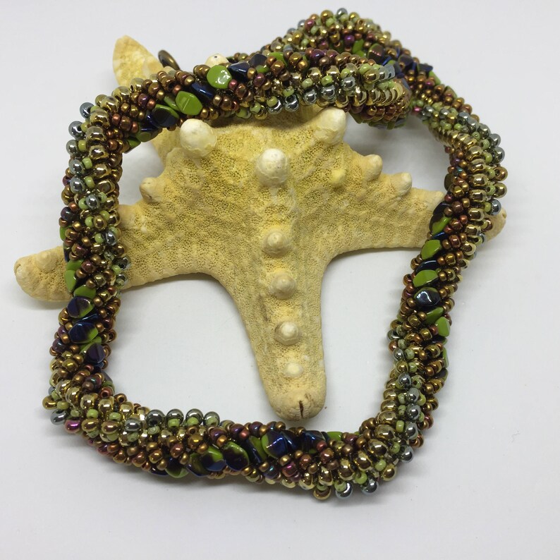 May include: A twisted beaded necklace with green, gold, silver, and purple beads. The necklace is coiled around a starfish.