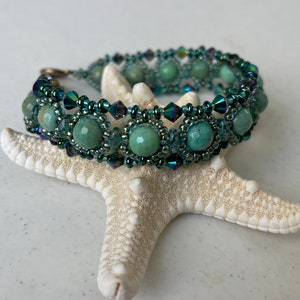 Könnte beinhalten: Ein grünes und blaues Perlenarmband mit einem silbernen Verschluss. Das Armband besteht aus runden grünen Perlen und kleinen blauen und silbernen Perlen.