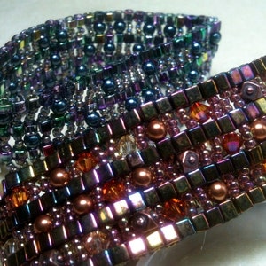 May include: Two beaded bracelets with iridescent, multi-colored beads. The top bracelet is a dark blue, green, and purple color. The bottom bracelet is a mix of brown, orange, and purple.