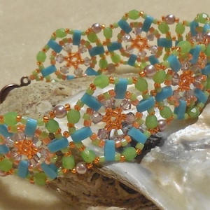 Könnte beinhalten: Ein Armband aus Perlen mit einem sich wiederholenden Muster aus türkisfarbenen, grünen und orangefarbenen Perlen. Das Armband ist aus kleinen Perlen und größeren, facettierten Perlen gefertigt. Das Armband wird auf einer weißen Muschel gezeigt.