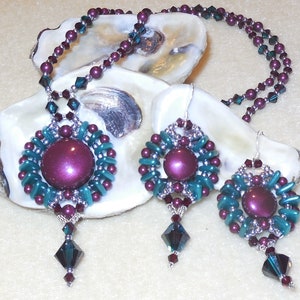 Puede incluir: Un conjunto de joyas de cuentas color turquesa y burdeos con un collar de colgante y pendientes a juego. El collar presenta una gran cuenta redonda de color burdeos rodeada de cuentas de color turquesa. Los pendientes son de diseño similar, con cuentas de color burdeos más pequeñas.