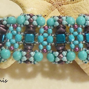 Op de afbeelding: Een turquoise en paarse kralen armband met een schuifsluiting. De armband is gemaakt met kleine, ronde kralen en heeft een geometrisch patroon.