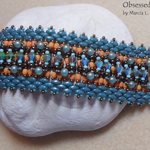 May include: A beaded bracelet with a turquoise, orange, and brown color scheme. The bracelet has a gold clasp and is labeled "Obsessed by Marcia L. Balonis".