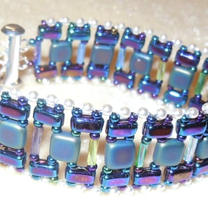 May include: A beaded bracelet with iridescent blue, purple, and green square beads, white round beads, and clear glass beads.