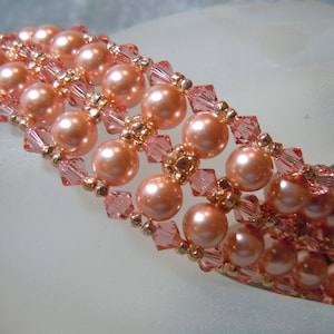 May include: A peach-colored beaded bracelet featuring rows of large, round faux pearls and smaller, square-cut crystals. The bracelet is accented with gold-toned beads, creating a delicate and elegant design. This jewelry piece is suitable for special occasions.