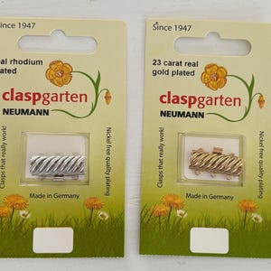 May include: Two packaging cards for clasps. The card on the left shows a silver clasp with the text "real rhodium plated claspgarten NEUMANN Clasps that really work! Made in Germany Nickel free quality plating". The card on the right shows a gold clasp with the text "23 carat real gold plated claspgarten NEUMANN Clasps that really work! Made in Germany Nickel free quality plating".