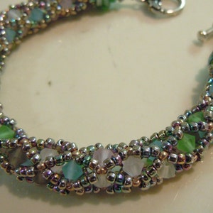 Puede incluir: Un brazalete de plata con un diseño tejido con cuentas iridiscentes de color verde, azul y rosa.