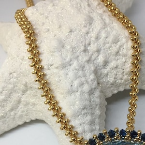 May include: A gold chain necklace with a blue and gold beaded pendant. The chain is made of small, round beads and the pendant is a circle with a blue center and a gold border.
