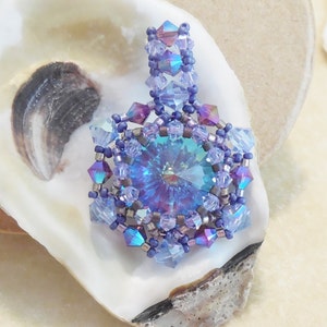 May include: A beaded pendant featuring a large iridescent blue crystal at its centre, surrounded by smaller iridescent blue and purple beads. The pendant hangs from a strand of iridescent blue beads.