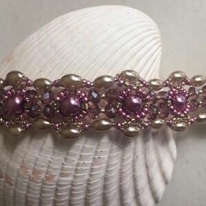 Op de afbeelding: Een delicate armband met een herhalend patroon van roze en gouden kralen. De armband is gemaakt met kleine, ronde kralen en grotere, ovale kralen.