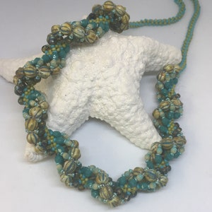 May include: A twisted beaded necklace with brown, beige, teal, and green beads. The necklace is displayed on a white starfish.
