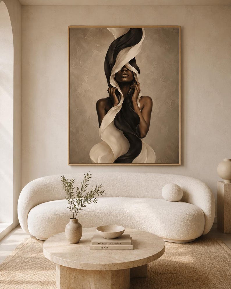 Peut inclure: Une &oelig;uvre d'art encadr&eacute;e repr&eacute;sente une femme avec un tissu noir et blanc fluide. L'&oelig;uvre est dans un cadre dor&eacute; et est suspendue au-dessus d'un canap&eacute; incurv&eacute; de couleur cr&egrave;me. Une table basse ronde avec des livres et un vase de verdure se trouve devant le canap&eacute;.