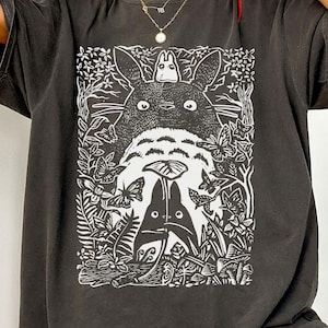 Puede incluir: Camiseta de color pimienta de gran tama&ntilde;o con un gr&aacute;fico blanco de una escena de bosque con una criatura grande, similar a un dibujo animado, y figuras m&aacute;s peque&ntilde;as. El texto "COLOR: PEPPER COMFORT COLORS" es visible.