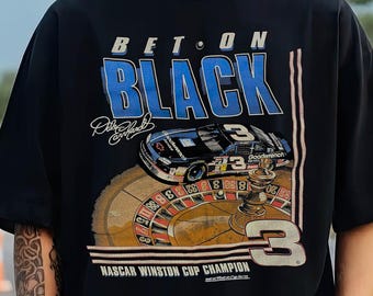 Puede incluir: Camiseta negra con un diseño gráfico que presenta el texto "BET ON BLACK" en blanco y azul, un coche de carreras y el número 3. La camiseta también incluye el texto "NASCAR Winston Cup Champion".