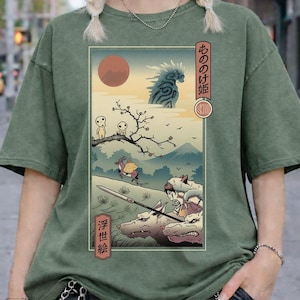 May include: Moss green comfort colors t-shirt featuring a Japanese anime-style graphic. The graphic depicts a scene with characters, a red sun, and Japanese text. The shirt has short sleeves and a relaxed fit.