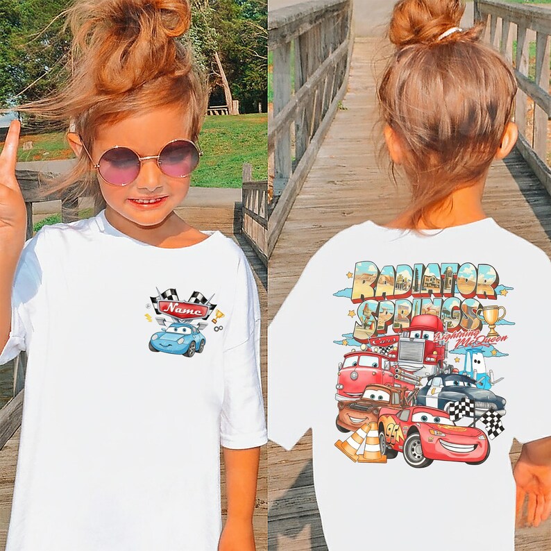 May include: White t-shirt with a cartoon car design. The front features a blue car and the word "Name". The back displays "Radiator Springs" with cartoon cars. The design is colourful and suitable for children.