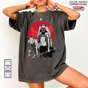 May include: Pepper-colored t-shirt featuring a graphic of a woman with a wolf, a red circle, and Japanese text. The design is in black and white with red accents. The shirt has short sleeves and a relaxed fit.