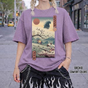 May include: Orchid-colored t-shirt featuring a Japanese anime-style illustration. The graphic depicts a scene with characters, a red sun, and text in Japanese. The shirt is part of the Comfort Colors collection.