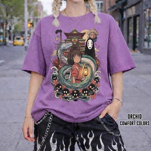 May include: Orchid purple t-shirt with a vibrant graphic from a Japanese animated film. The design features a girl, a dragon, and other characters. The text "ORCHID COMFORT COLORS" is printed on the lower right side.