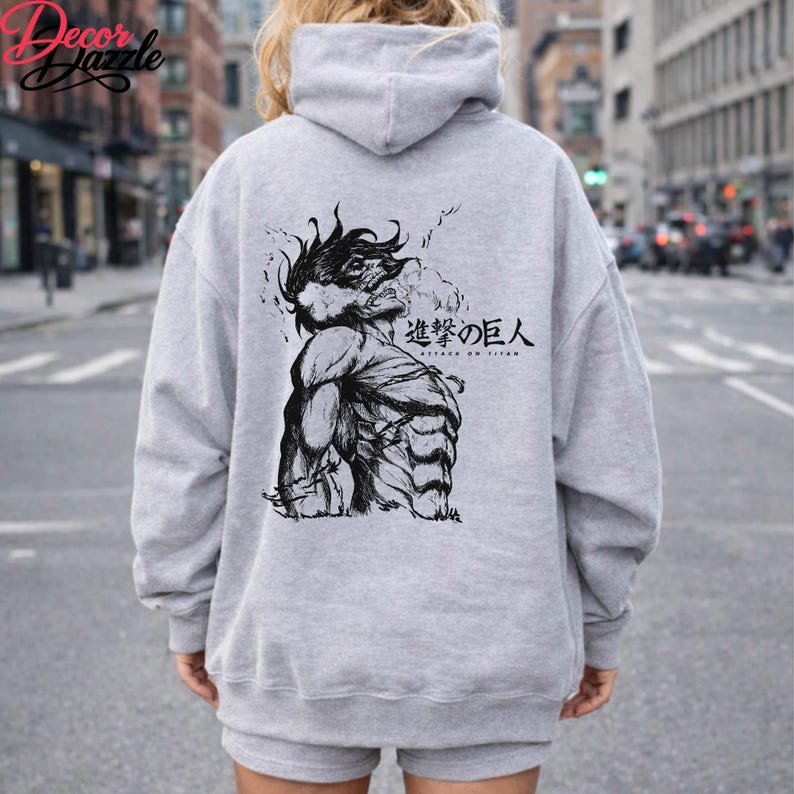 May include: A light gray hoodie featuring a black and white illustration of a muscular figure with the text "Attack on Titan" in Japanese. The hoodie has a hood and long sleeves.