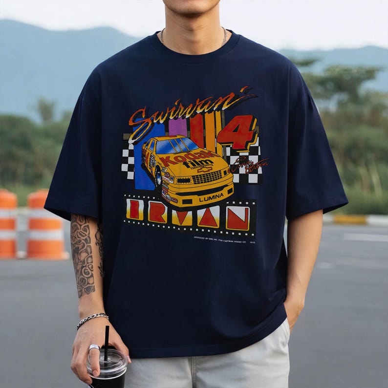May include: Navy blue t-shirt with a vintage racing car graphic. The design features a yellow race car with "Kodak Film" branding, the number "4", and the text "Swirvan" and "IRVAN". The shirt has a classic, relaxed fit.