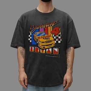 May include: Dark gray t-shirt featuring a vintage-style graphic of a yellow race car with the text "Swirvin' 4" and "Kodak film". The design includes checkered flags and the word "Lumina".