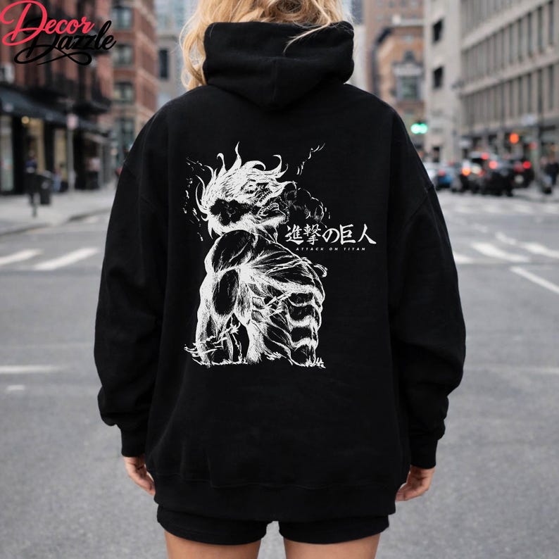 May include: Black hoodie featuring a white graphic of a muscular figure with the Japanese text "Attack on Titan". The hoodie has a drawstring hood and long sleeves. The image is centered on the back of the hoodie.