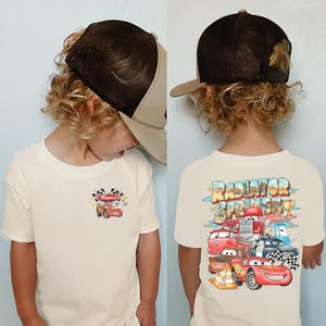 May include: A beige t-shirt with a cartoon car design and the text "Name" and a checkered flag. The back of the shirt features a colourful graphic of cars with the words "Radiator Springs Lightning McQueen".