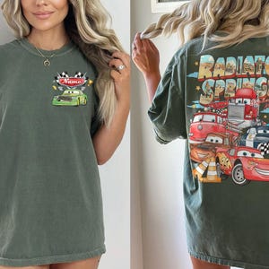 May include: Dark green t-shirt with a front graphic of a green race car and the name "Name", and a back graphic of cartoon cars with the text "Radiator Springs". The shirt has short sleeves and a loose fit.