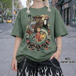 May include: Moss green t-shirt with a vibrant graphic from a Japanese animated film. The design includes a girl with a lantern, a dragon, and other characters. The text "MOSS COMFORT COLORS" is printed on the lower right.