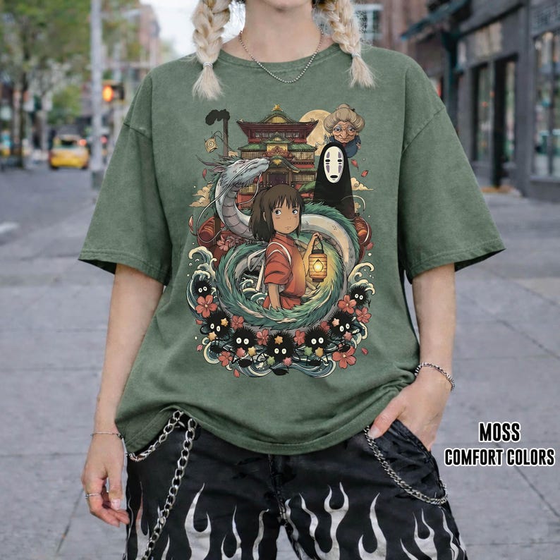 May include: Moss green t-shirt with a vibrant graphic from a Japanese animated film. The design includes a girl with a lantern, a dragon, and other characters. The text "MOSS COMFORT COLORS" is printed on the lower right.