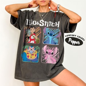 May include: Dark gray t-shirt featuring the words "Lilo & Stitch" above four cartoon character images. The shirt has a distressed look and the words "Comfort Colors Pepper" are printed on the right side.