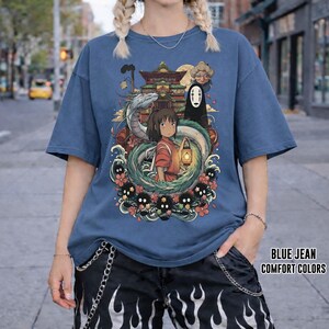 May include: Blue jean coloured t-shirt featuring a graphic from a Japanese animated film. The graphic shows a girl with a lantern, a dragon, and other characters. The text "BLUE JEAN COMFORT COLORS" is printed on the bottom right.