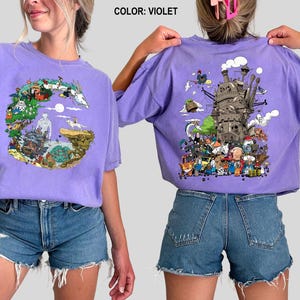 Op de afbeelding: Violet T-shirt met korte mouwen met een kleurrijk grafisch ontwerp op de voor- en achterkant. Het ontwerp aan de voorkant is een cirkelvormige illustratie met personages en landschappen. Het ontwerp aan de achterkant toont een gedetailleerde illustratie van een kasteel en personages.
